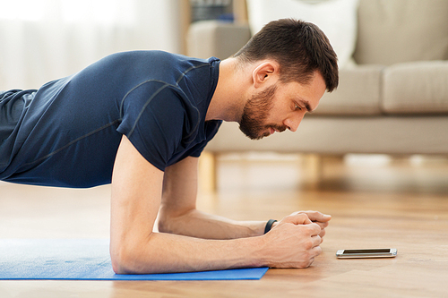 sport, fitness and healthy lifestyle concept - man looking at smartphone and doing plank exercise at home