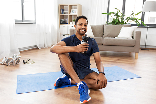 fitness, sport and healthy lifestyle concept - smiling indian man drinking water after training at home