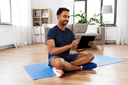 sport, technology and healthy lifestyle concept - smiling indian man with tablet computer sitting on exercise mat at home