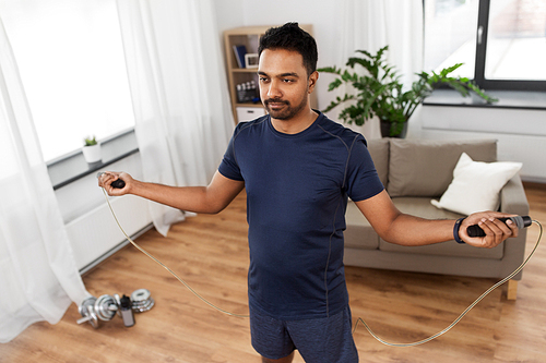 fitness, sport, exercising and healthy lifestyle concept - indian man skipping with jump rope at home