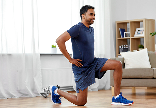 sport and healthy lifestyle concept - indian man with fitness tracker exercising and doing squats at home