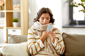 people, health and medicine concept - sad sick woman in scarf with pills at home