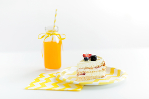 party food, junk-food and sweets concept - piece of delicious berry layer cake on disposable plate, paper napkin and orange juice in bottle over white background