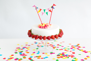 food, dessert and party concept - close up of birthday cake with candies, garland and strawberries on stand