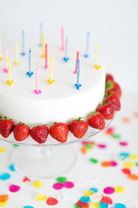 food, dessert and party concept - close up of birthday cake with candles and strawberries on stand