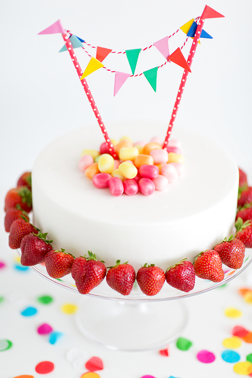 food, dessert and party concept - close up of birthday cake with candies, garland and strawberries on stand