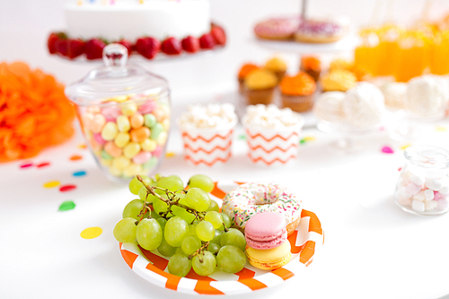 food and festive concept - grapes, macarons and donut on party table