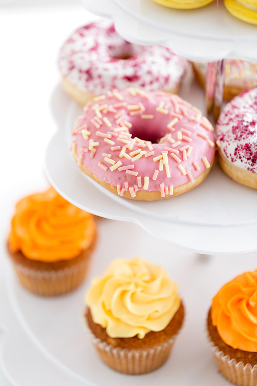 fast food, dessert and sweets concept - close up of glazed donuts and cupcakes on stand