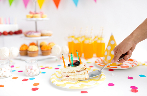 food, celebration and festive concept - hand with shovel putting piece of cake with candles on plate at birthday party