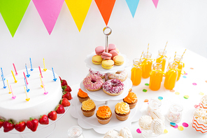 party and festive concept - birthday cake with candles and strawberries, drinks and food on table