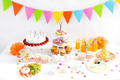 party and festive concept - birthday cake with candles and strawberries, garland, drinks and food on table