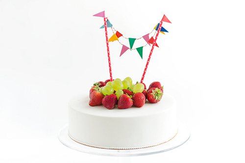 food, dessert and party concept - close up of birthday cake with garland, strawberries and grapes on stand