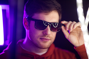 leisure, clubbing and nightlife concept - portrait of smiling young man in sunglasses at dark room over ultra violet neon lights of night club