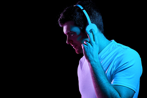 music, technology and people concept - portrait of young man in wireless headphones over ultra violet neon lights in dark room of night club