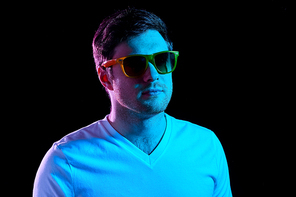 leisure, clubbing and nightlife concept - portrait of young man in sunglasses at dark room over ultra violet neon lights