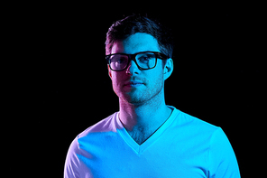 people concept - portrait of young man in glasses and t-shirt over ultra violet neon lights in dark room