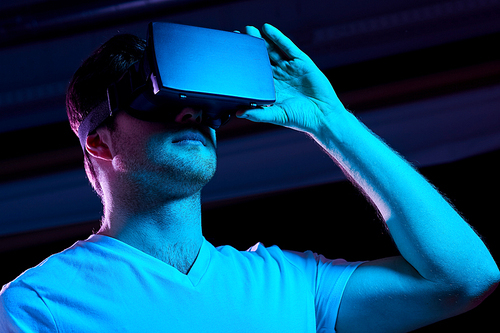 3d technology, virtual reality, entertainment and people concept - young man in vr glasses playing game over ultra violet neon lights in dark room