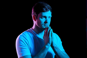 faith, religion and people concept - young man praying god over ultra violet neon lights in dark room