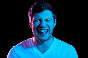 emotion, expression and people concept - portrait of laughing young man in t-shirt over ultra violet neon lights in dark room
