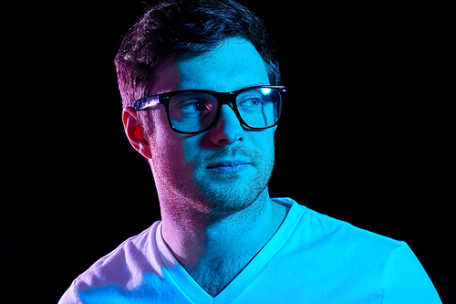people concept - portrait of young man in glasses and t-shirt over ultra violet neon lights in dark room