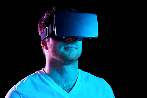 3d technology, virtual reality, entertainment and people concept - young man in vr glasses playing game over ultra violet neon lights in dark room