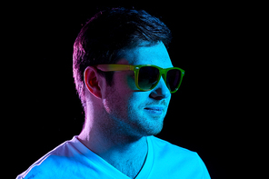 leisure, clubbing and nightlife concept - portrait of young man in sunglasses at dark room over ultra violet neon lights