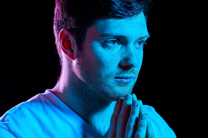 faith, religion and people concept - close up of young man praying god in dark room with ultra violet neon lights