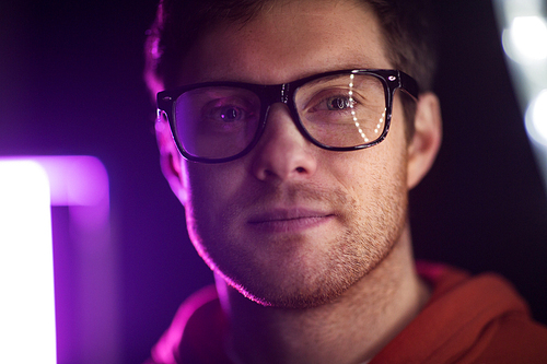 vision, eyewear and people concept - portrait of smiling young man in glasses over ultra violet neon lights in dark room