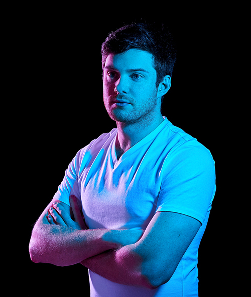 people concept - portrait of young man in t-shirt with crossed arms over ultra violet neon lights in dark room