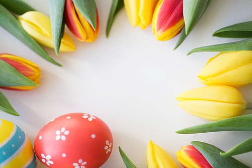 easter, holidays, tradition and object concept - close up of colored easter eggs and tulip flowers on white background
