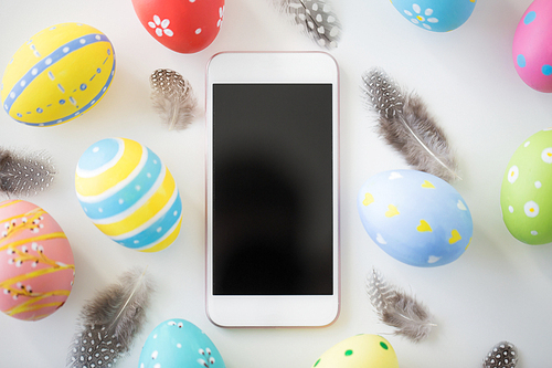 easter, holidays and object concept - close up of colored eggs and feathers on white background