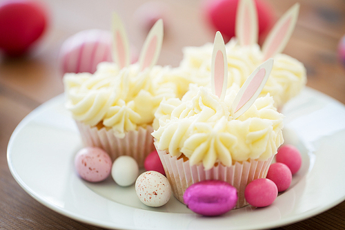 easter, food and holidays concept - frosted cupcakes with colored eggs and candies on plate