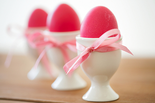 easter and holidays concept - pink colored eggs in ceramic cup holders with ribbons on table
