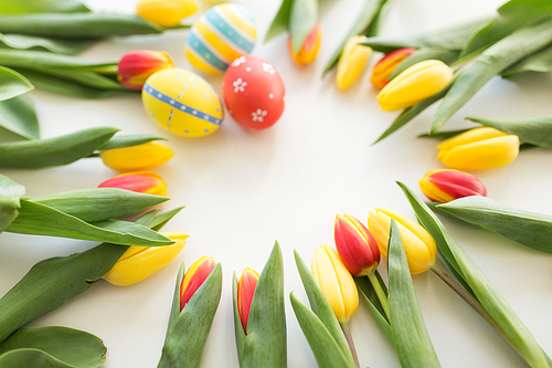 easter, holidays, tradition and object concept - close up of colored easter eggs and tulip flowers on white background