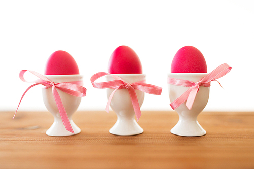 easter and holidays concept - three pink colored eggs in ceramic cup holders with ribbons on table