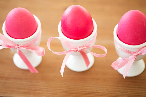 easter and holidays concept - pink colored eggs in ceramic cup holders with ribbon on table
