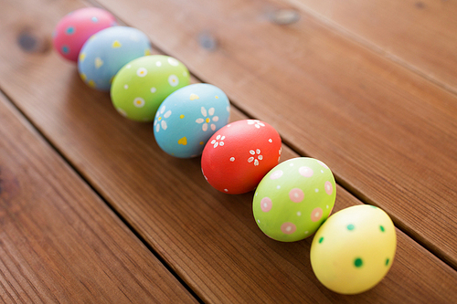 easter, holidays and tradition concept - row of colored eggs on wooden table