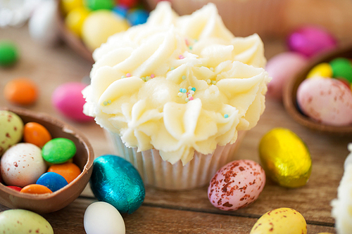 easter, food and sweets concept - frosted cupcakes with chocolate eggs and candies on table