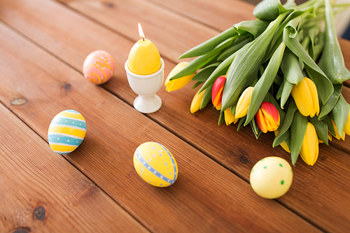 easter, holidays, tradition and object concept - burning candle, colored eggs and tulip flowers on wooden table