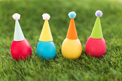 easter, holidays, tradition and object concept - row of colored eggs in party hats on artificial grass