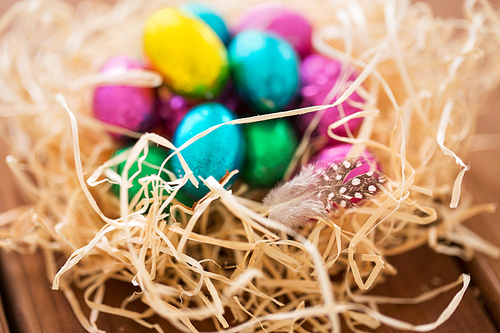 easter, confectionery and holidays concept - chocolate eggs in straw nest on wooden table