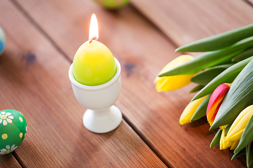 easter, holidays, tradition and object concept - burning candle in shape of egg and tulip flowers on wooden table
