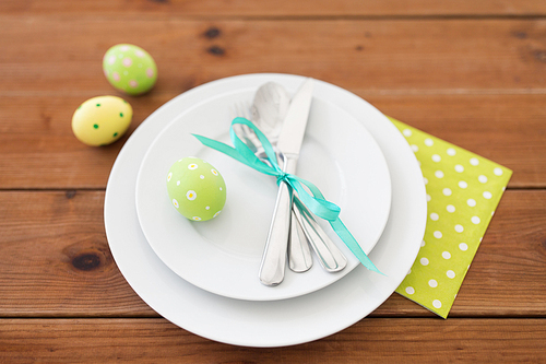 easter, holidays, tradition and object concept - green colored egg in cup holder, plates and cutlery on table at home