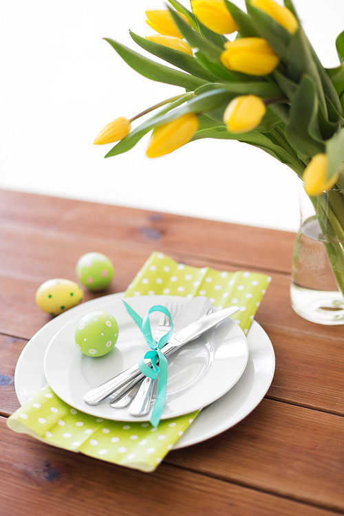easter, holidays, tradition and object concept - green colored egg, plates with cutlery and tulip flowers on table at home