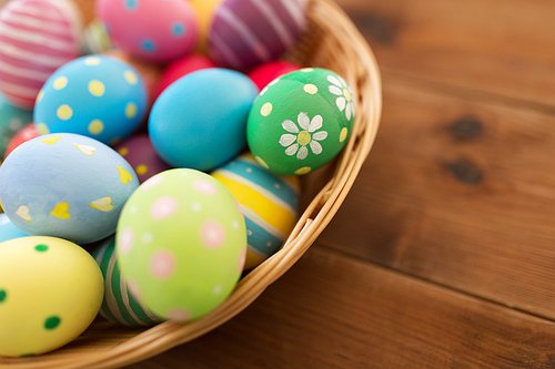 easter, holidays and tradition concept - close up of colored eggs in basket on wooden table