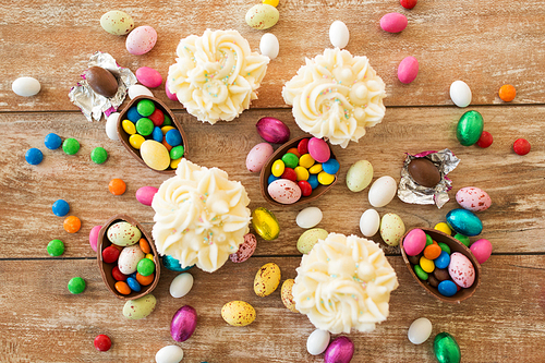 easter, food and holidays concept - frosted cupcakes with chocolate eggs and candies on wooden table