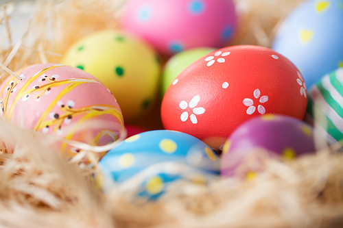 easter, holidays, tradition and object concept - close up of colored eggs in straw