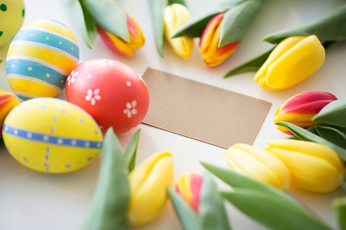 easter, holidays, tradition and object concept - close up of colored eggs and tulip flowers on white background