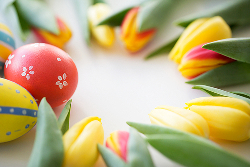 easter, holidays, tradition and object concept - close up of colored eggs and tulip flowers on white background