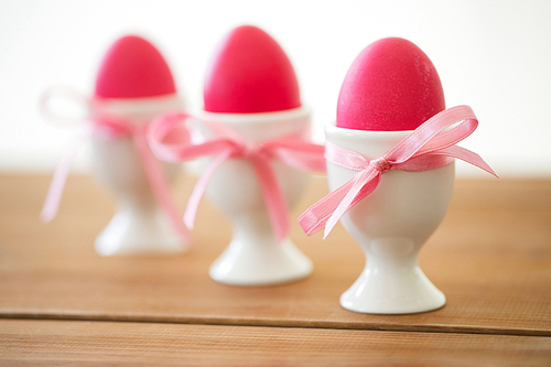 easter and holidays concept - pink colored eggs in ceramic cup holders with ribbons on table
